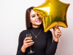 empath woman in black dress with gold star shaped balloon drinking champagne